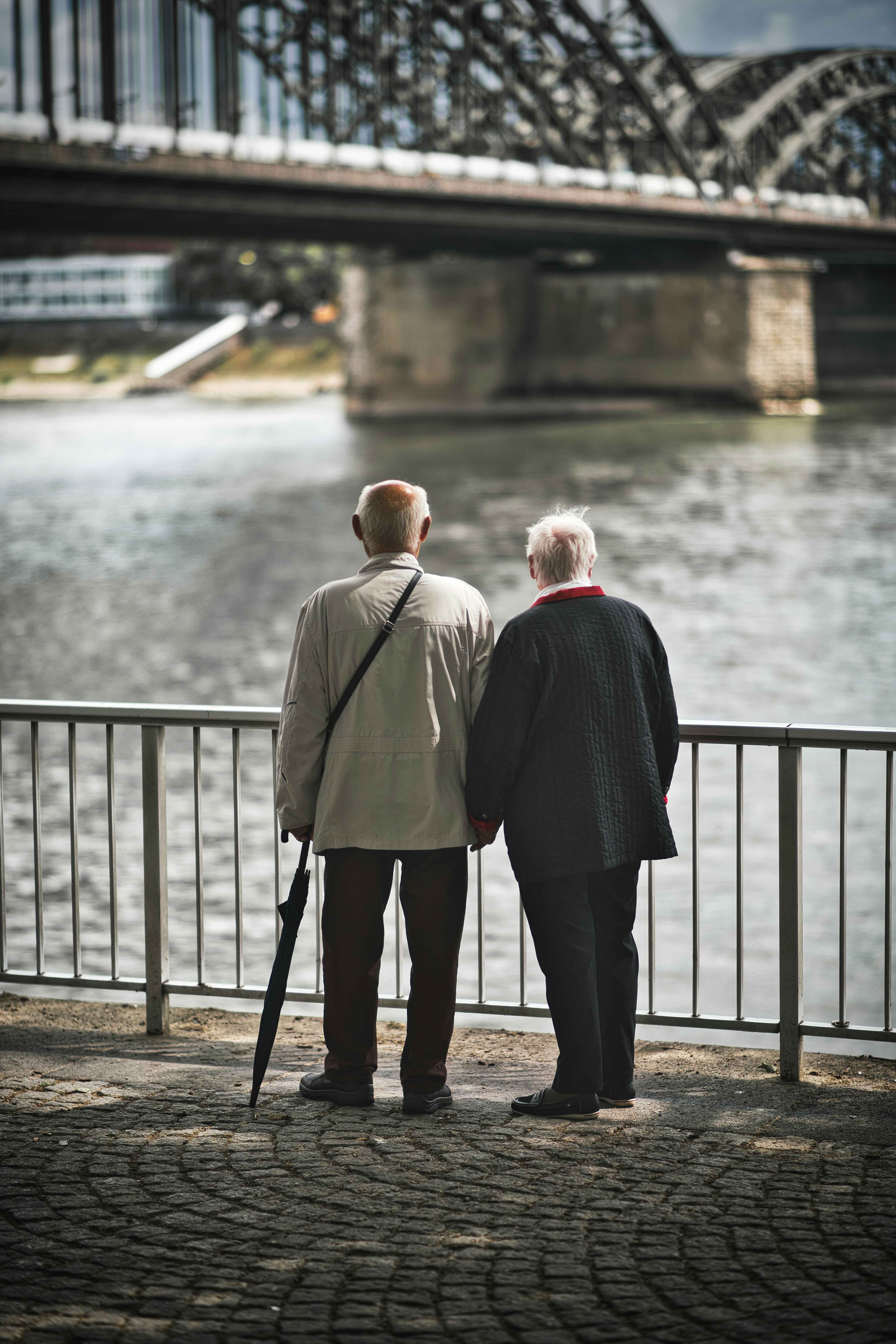 Couple de retraités se tenant la main au bord de l’eau, de dos