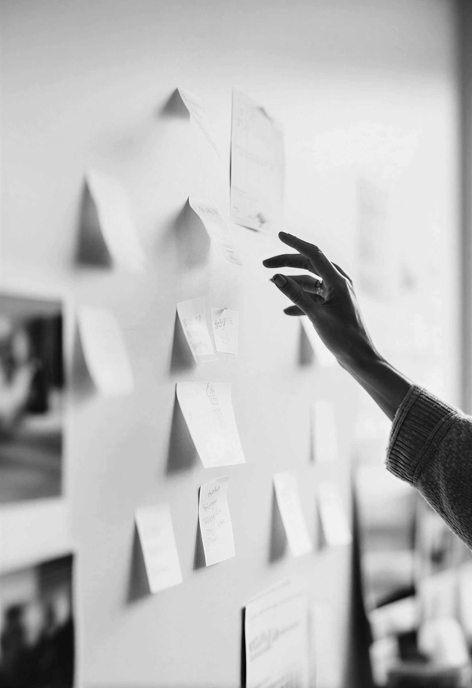 Main qui organise des notes autocollantes sur un mur, image en noir et blanc